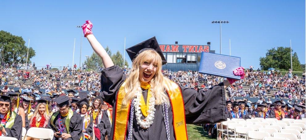 A student at commencement holding up her diploma wearing the womens and gender studies pink gloves