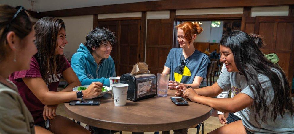 Five students in the dining hall, around a cafe table