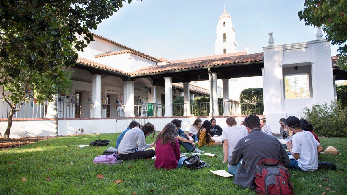 A class meeting outside on the grass with the SMC chapel in the background