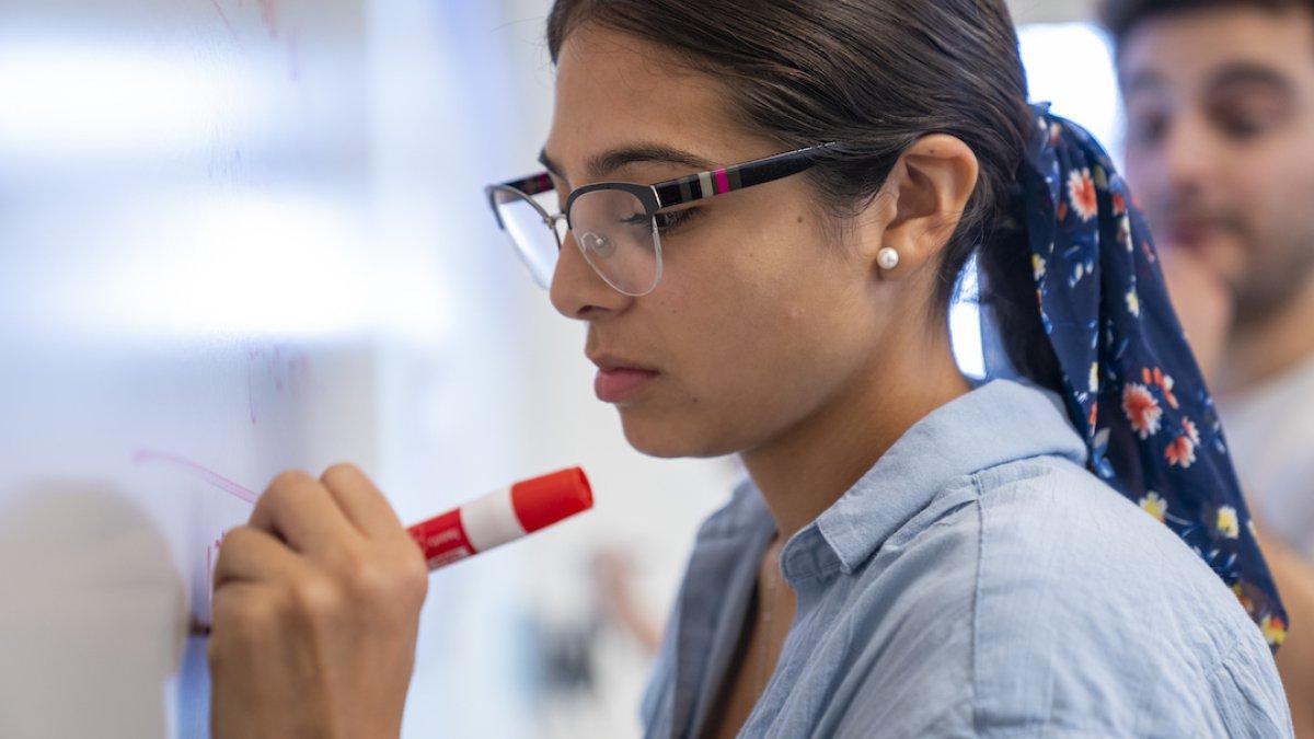 A student is standing up, writing on a whiteboard 